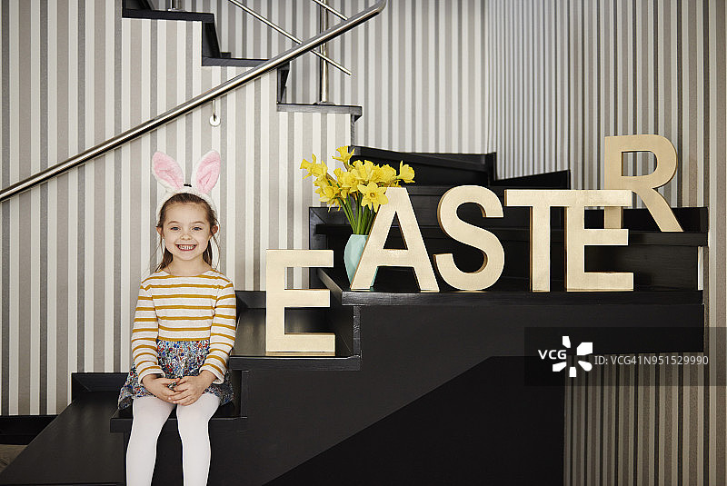 微笑的兔耳朵女孩坐在楼梯上的肖像，旁边是“复活节”图片素材