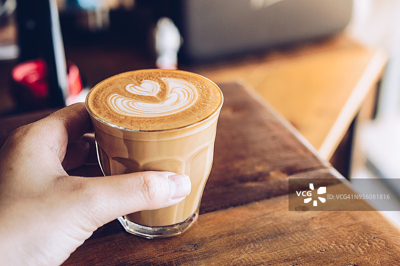 特写的一个人的手触摸一杯热拿铁咖啡在咖啡馆。图片素材