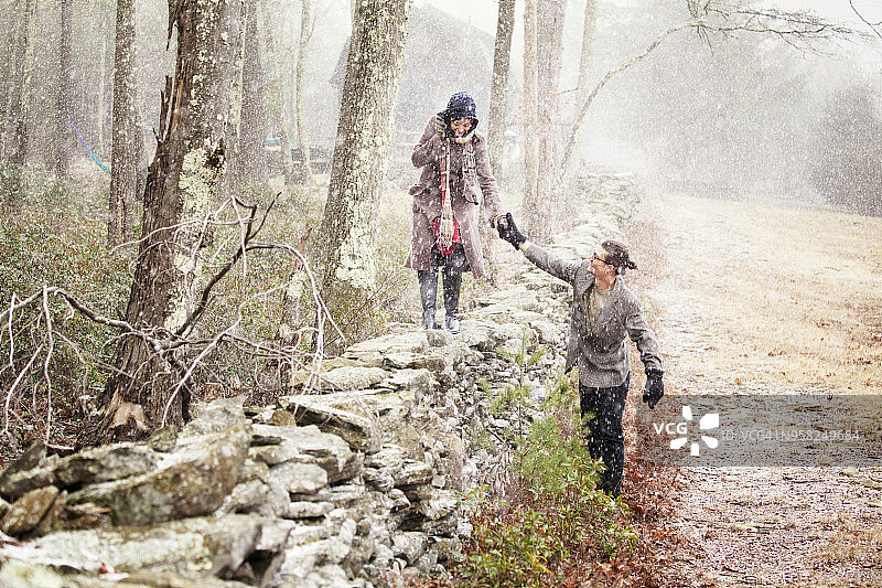 男人在冬天帮助女人在石墙上行走图片素材