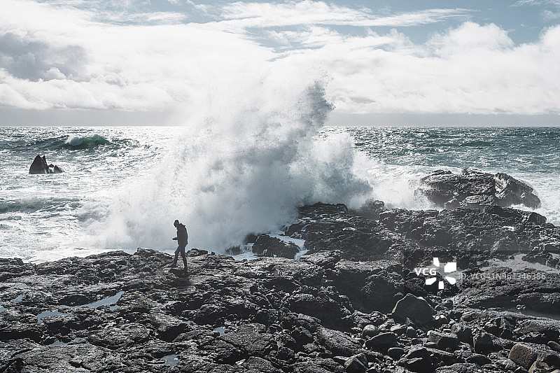 全长的徒步旅行者对抗海浪拍打在海滩上的岩石图片素材