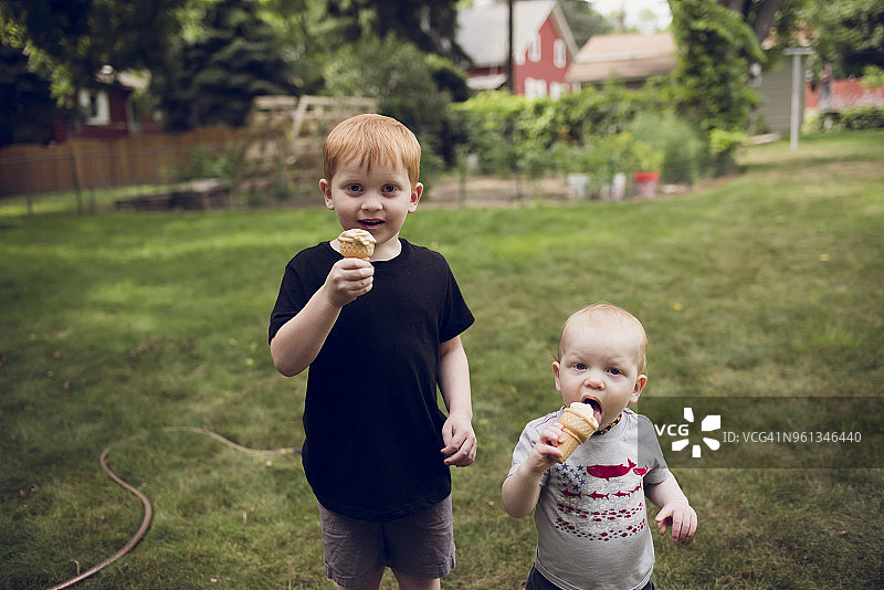 兄弟们站在公园的草地上吃甜筒冰淇淋的肖像图片素材