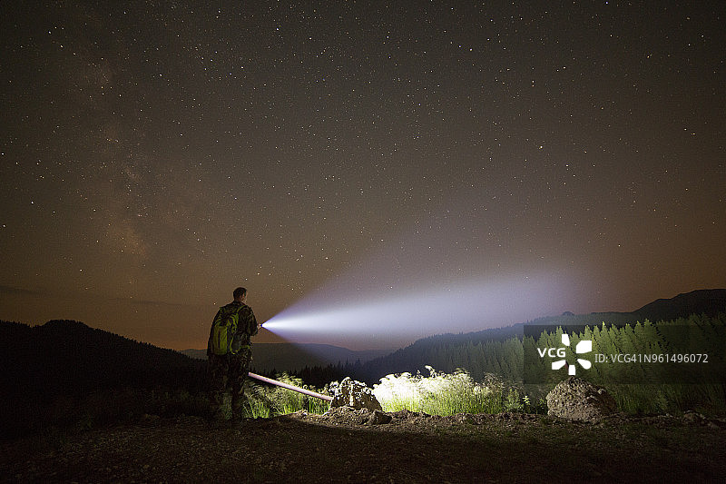 在星光灿烂的天空下，站在山上的徒步旅行者用手电筒照明图片素材