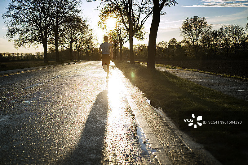 在日落时在公路上跑步的男运动员的后视图图片素材