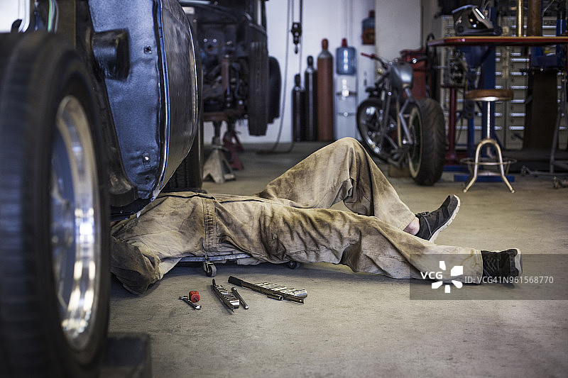 在汽车修理厂，修理工在车下工作时爬行小车的侧面图图片素材