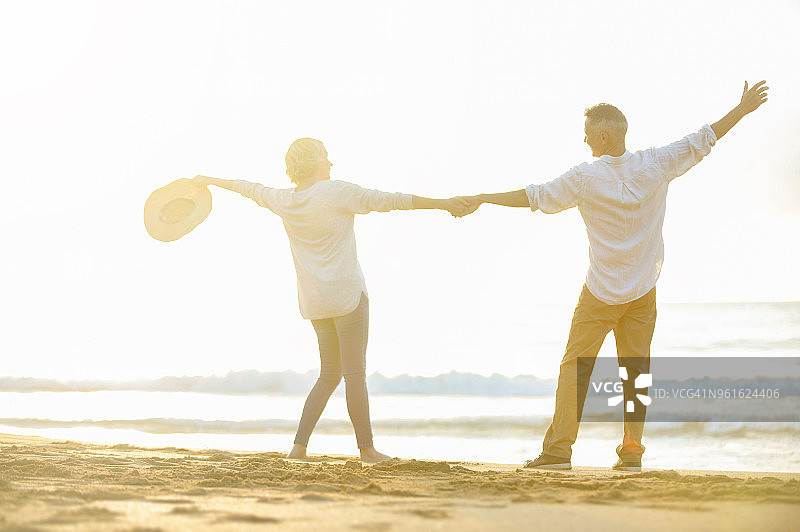 日出或日落时，情侣们手牵着手在海滩上跳舞。图片素材