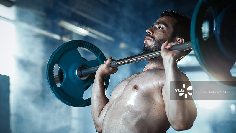 一个肌肉赤裸的男人举起沉重的杠铃和在工业健身房大楼做军事压健美锻炼的特写。图片素材