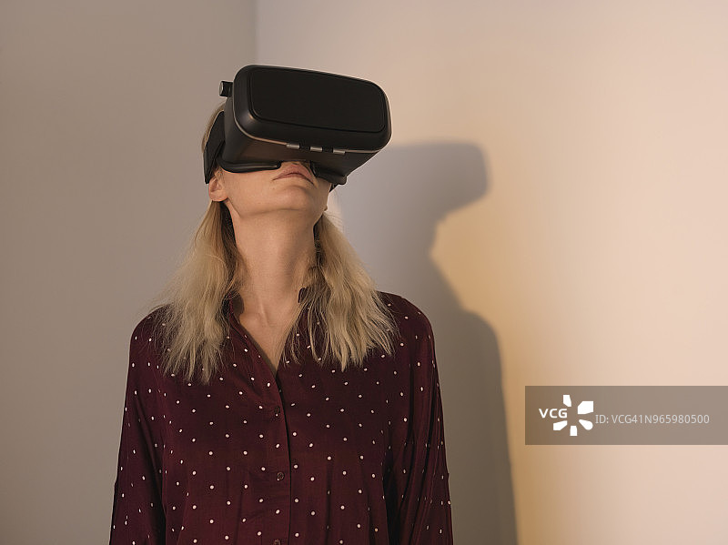 在家靠墙站着的妇女使用虚拟现实模拟器图片素材
