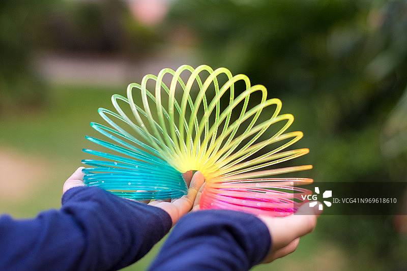 女孩玩彩虹色的电线螺旋玩具在白色的背景。图片素材