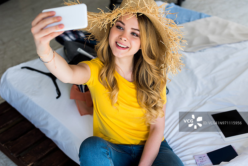 迷人的微笑女孩戴着草帽在智能手机上自拍图片素材