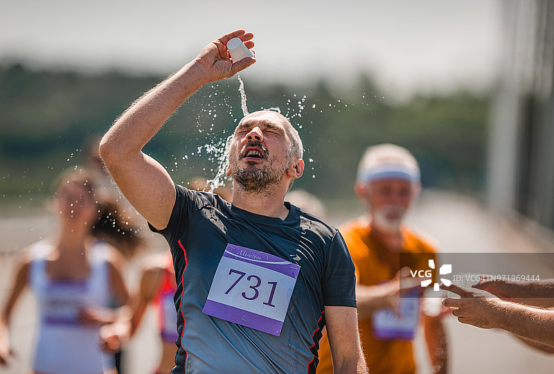 在马拉松比赛中，精疲力竭的男运动员将清水倒在头上。图片素材