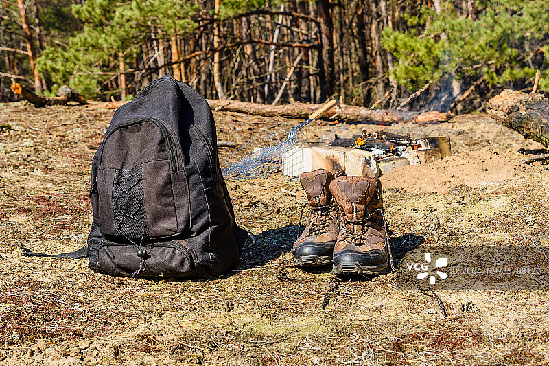 背包和旅游靴在一个针叶林的地面上。篝火的背景图片素材