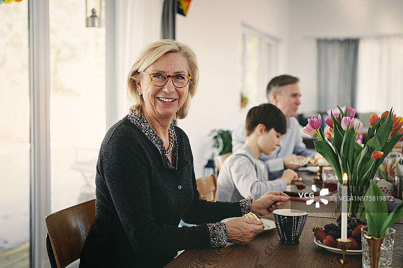 微笑的祖母坐在餐桌上与家人在聚会期间的肖像图片素材