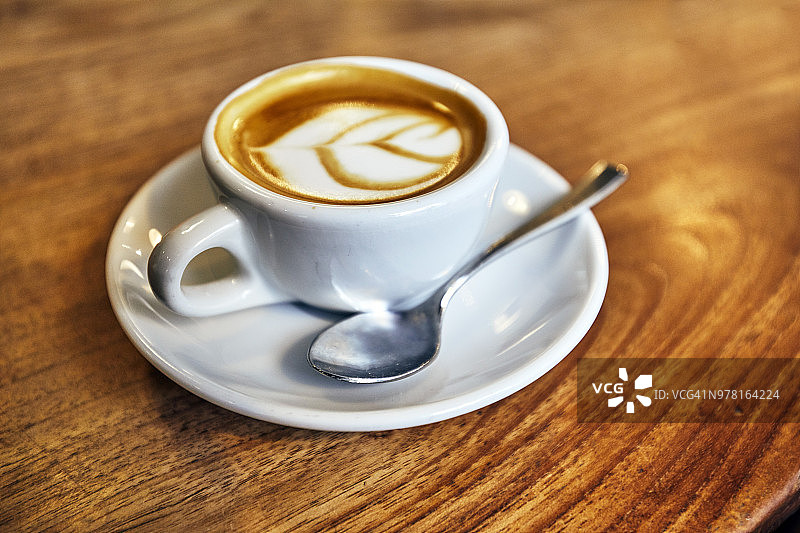 新鲜煮好的咖啡，意式浓缩咖啡，玛奇朵咖啡，放在小的白色咖啡杯里，白色碟和金属勺子放在木桌上图片素材
