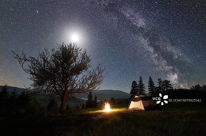 晚上在山上露营。游客帐篷篝火附近的森林在蓝色星空下，银河图片素材