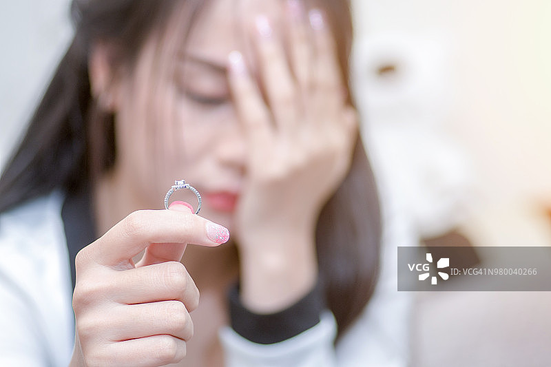 一个单身悲伤的妻子在离婚后手持结婚戒指悲叹的特写。图片素材
