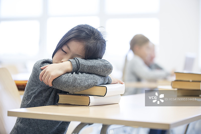 一个女学生在学校桌子上的一堆书上睡觉图片素材