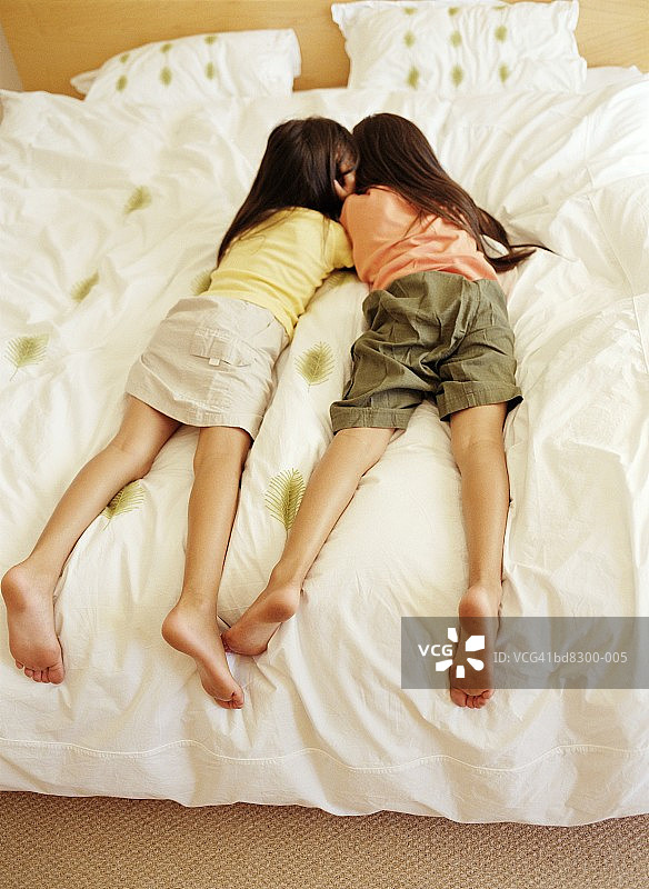 两个女孩(6-8)躺在床上，后视图图片素材
