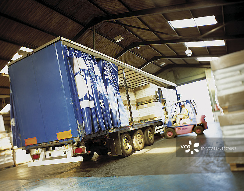 英国亨伯赛德郡的明汉港，一名男子在仓库里用叉车装载一辆铰接式货运卡车图片素材