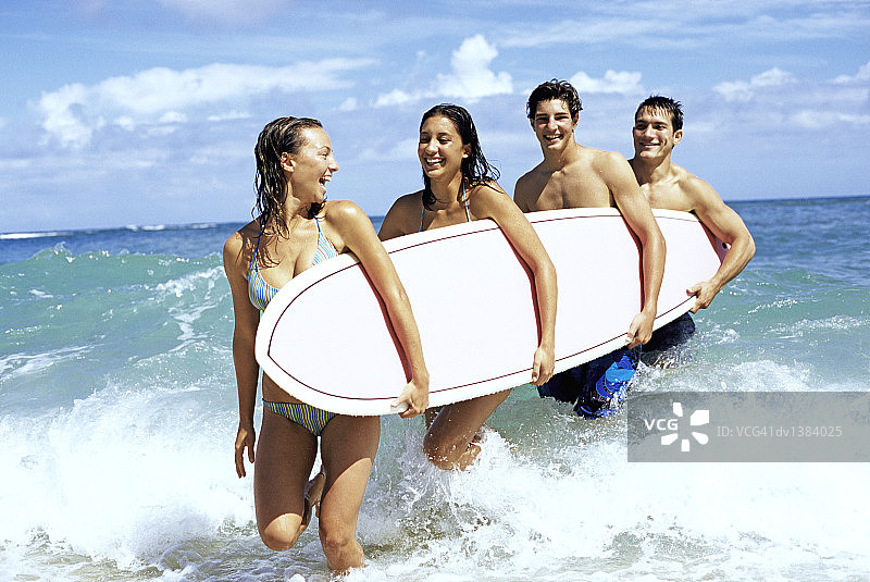 四个青少年朋友在海里跑步，胳膊下夹着一个冲浪板图片素材
