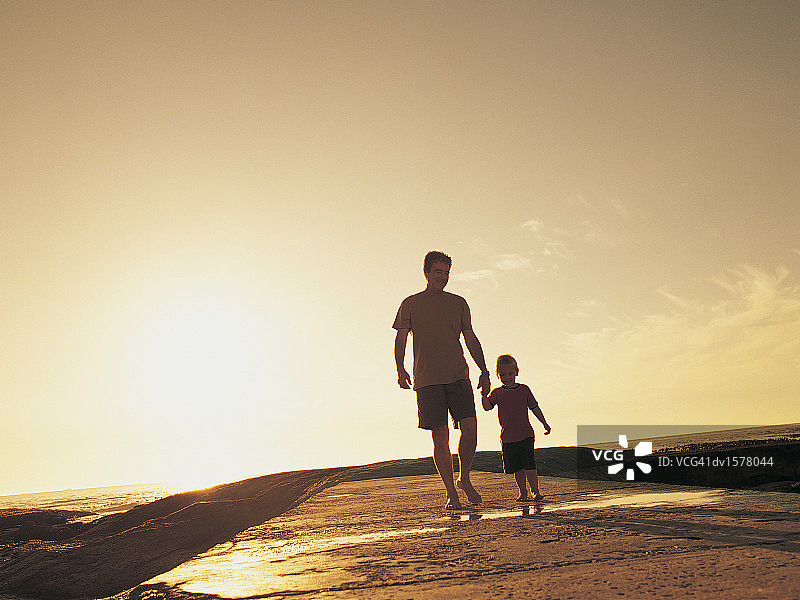 男孩和他的父亲在阳光下的海滩上散步图片素材