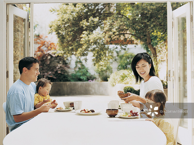 四口之家在一张朝庭院开着落地窗的桌子上用餐图片素材