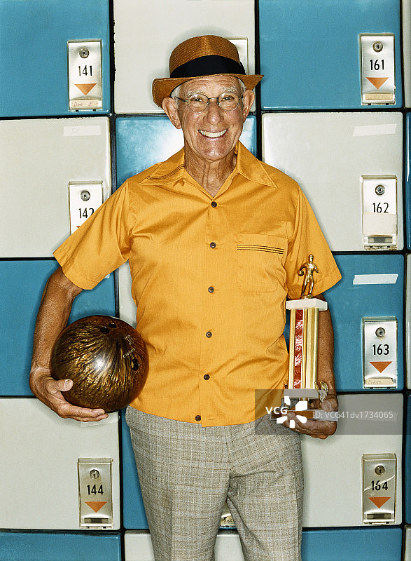 穿着黄色衬衫和帽子的老人，拿着一个保龄球和奖杯图片素材