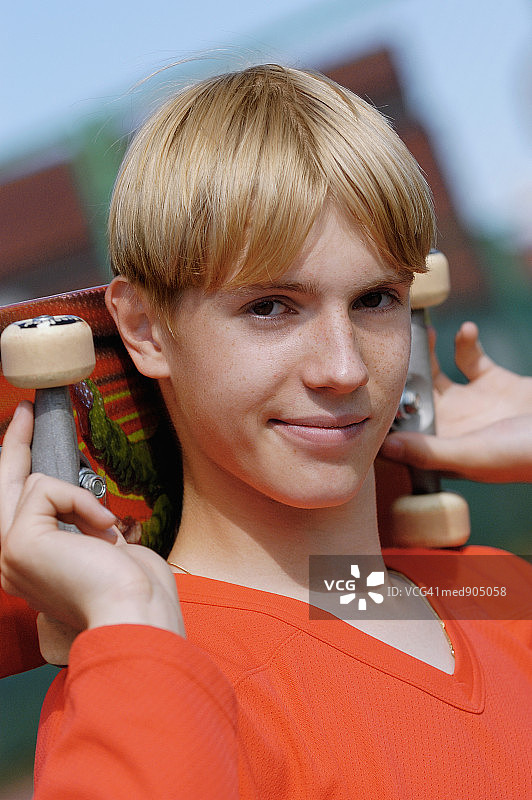 一个十几岁的男孩肩上扛着滑板的肖像图片素材
