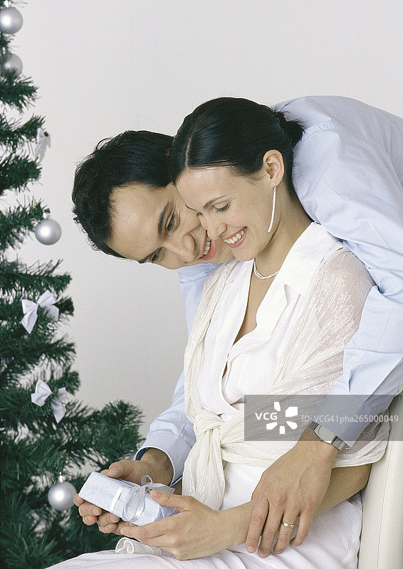 女人拿着礼物，男人弯着腰，身后是圣诞树图片素材