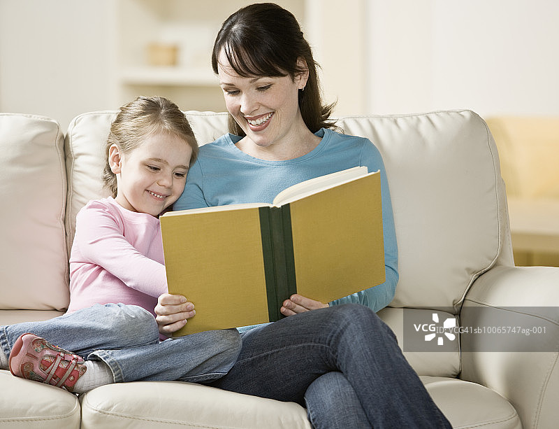 母亲带着4-5岁的女儿坐在沙发上看书图片素材