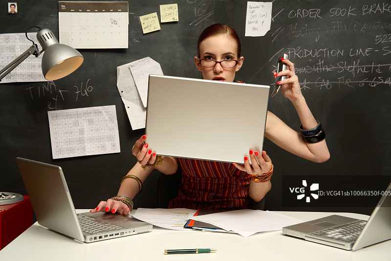 年轻女子用三台笔记本电脑用四只手，面带微笑，画像图片素材