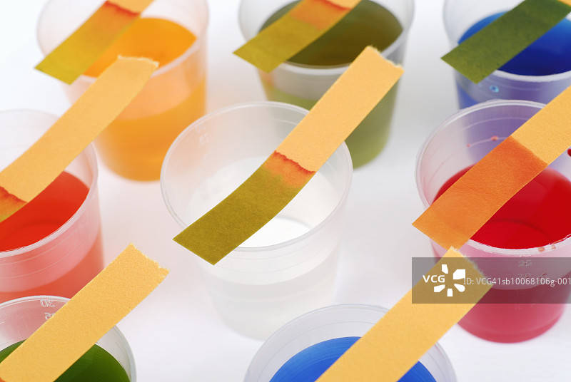 石蕊试纸贴在装有各种不同颜色液体的塑料杯上，拍摄工作室图片素材