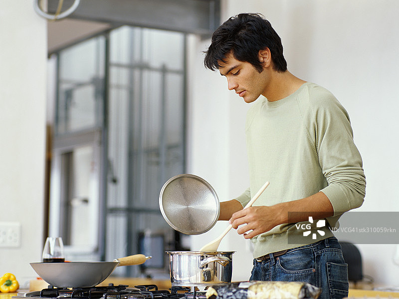 一个年轻人在厨房做饭的侧面图图片素材