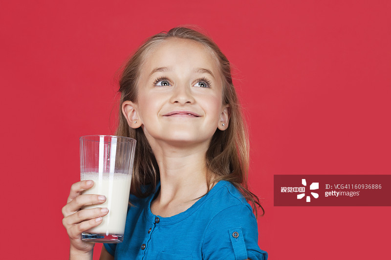 小女孩拿着牛奶杯，抬头看着红色的背景图片素材