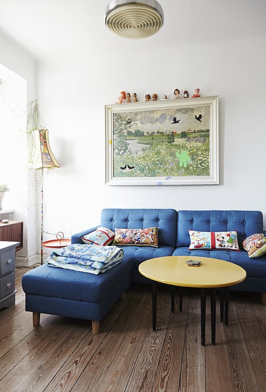 在简单的客厅里，黄色的桌面，蓝色的沙发，搭配长椅，墙上挂着画图片下载