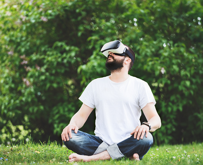 留着胡子的年轻男子戴着虚拟现实眼镜坐在花园里。生活方式VR的乐趣和…图片下载