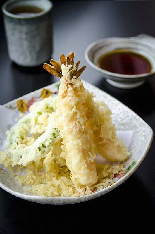 日式日式天妇罗配蔬菜和虾，用清淡的天妇罗面糊炸过，放在盘子里，黑色的桌子上，配以日式鱼汤蘸酱和绿茶图片下载