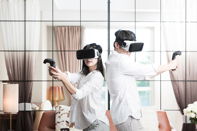 青年情侣在起居室一起玩VR虚拟游戏图片素材