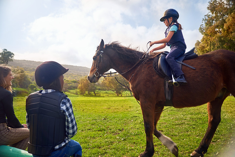女孩在农村的草地上学习骑马图片素材