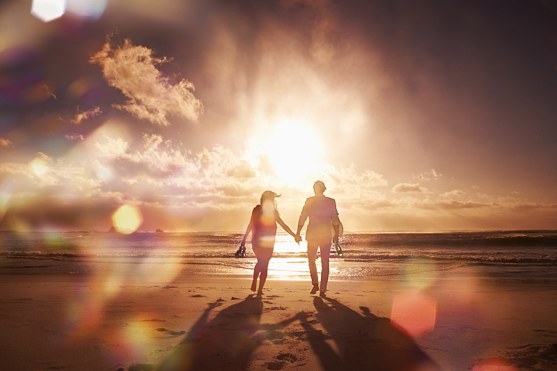 一对情侣在海滩上散步，夕阳下的剪影图片下载