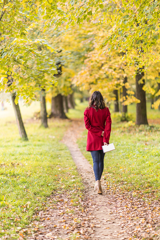 秋天里，一名年轻女子穿着便服在小路上散步图片下载