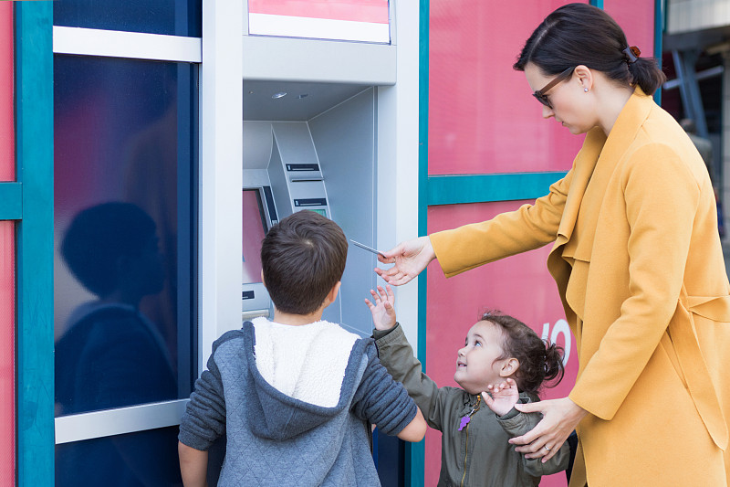 一位女士在城市里和孩子们站在一起时使用自动取款机图片素材