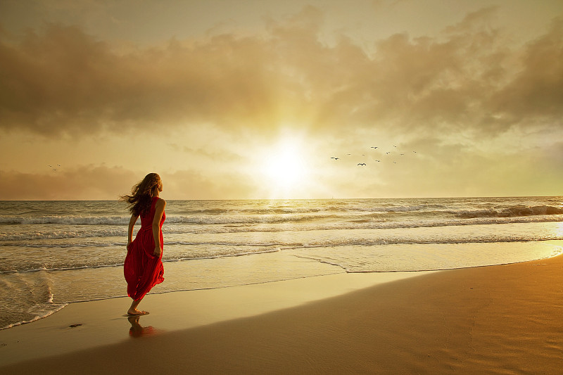 迷人的女人穿着美丽的衣服在海滩上日落图片素材