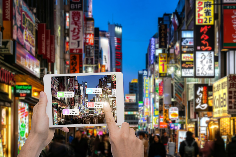 手持平板使用AR应用程序检查客户周围空间的相关信息。背景中的东京。图片素材