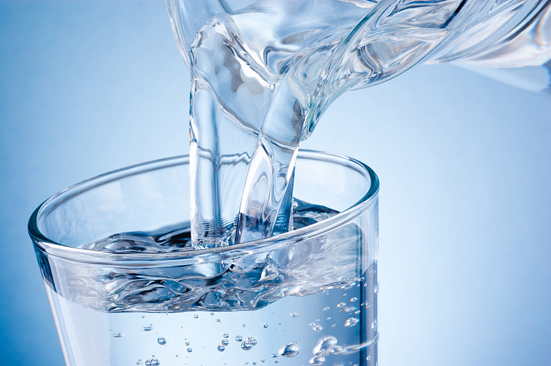 将水从水罐倒入蓝色背景的玻璃杯中图片下载