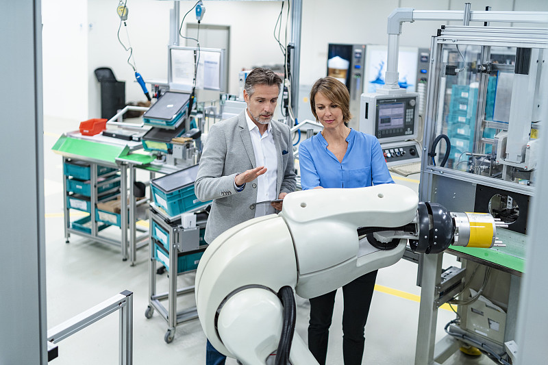商人与平板电脑和女人在工厂组装机器人交谈图片下载