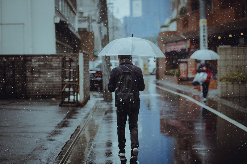一个年轻人撑着伞在城市街道的雪中行走图片下载