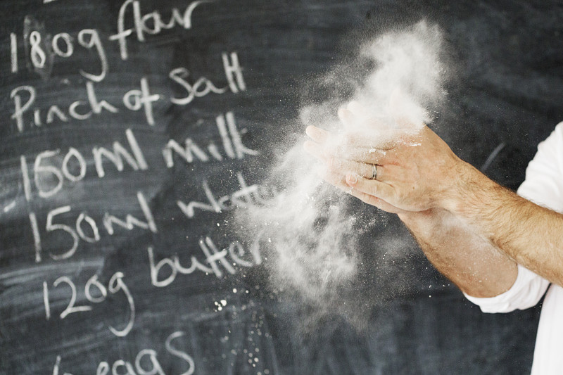 一个面包师站在黑板前的特写，他的手与面粉。图片下载