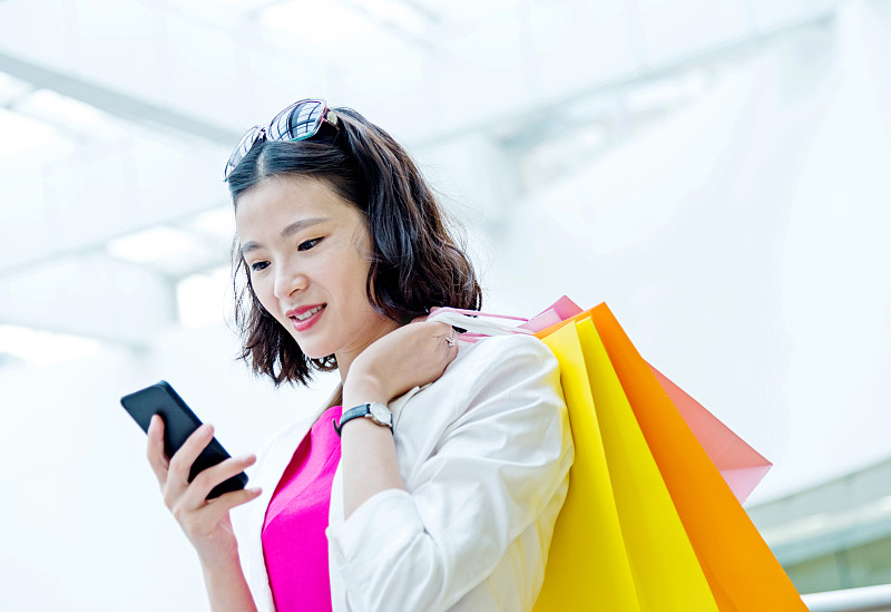 年轻的亚洲女人购物和发短信图片下载