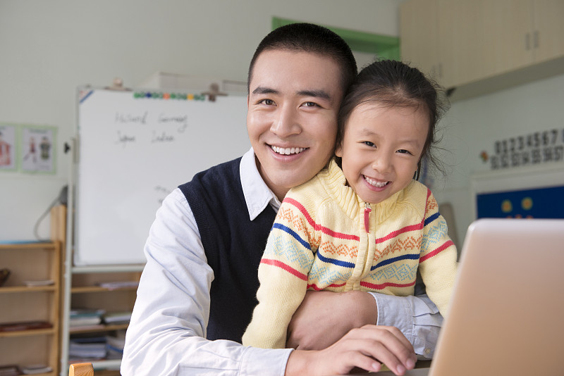 Kindergarten teacher and girl using laptop图片下载