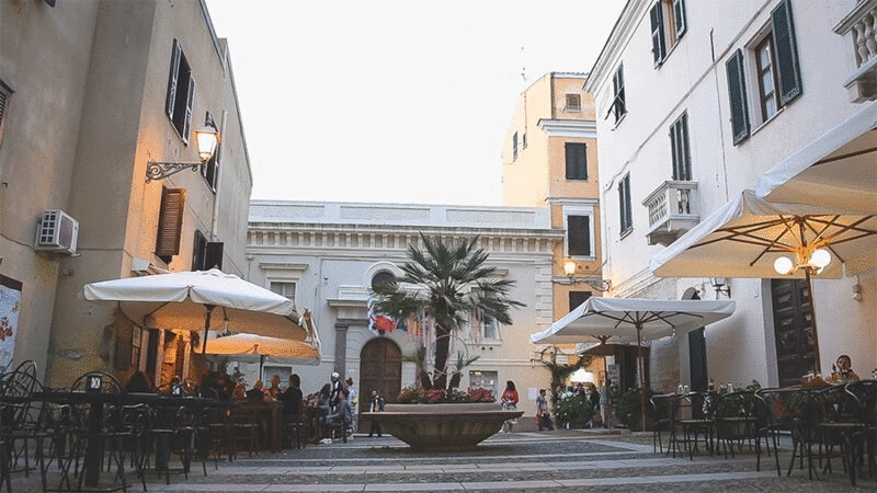 撒丁岛阿尔盖罗，带有户外餐厅和随风飘扬的旗帜的小广场图片下载